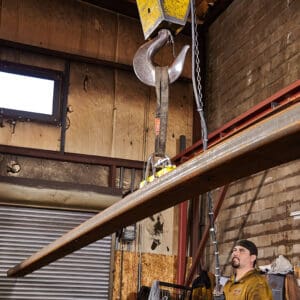 Worker guiding suspended metal beam indoors.