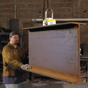 Worker handling large steel beam indoors.