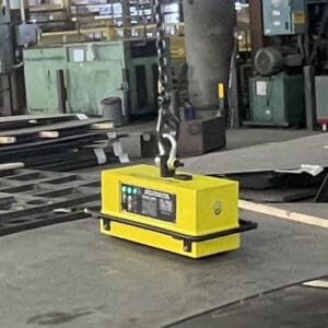 Yellow magnet lifting sheet metal in factory.