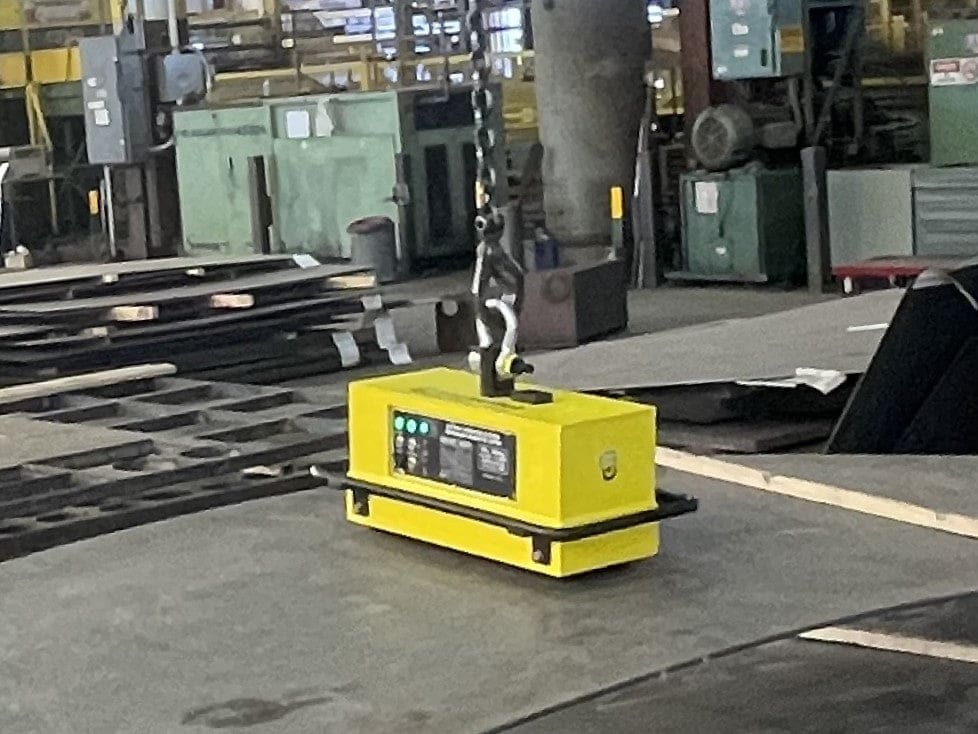 Yellow magnet lifting sheet metal in factory.