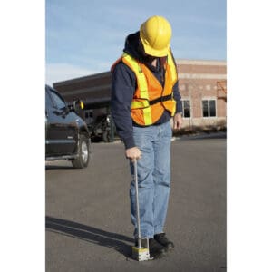 Worker using a magnetic sweeper on pavement.