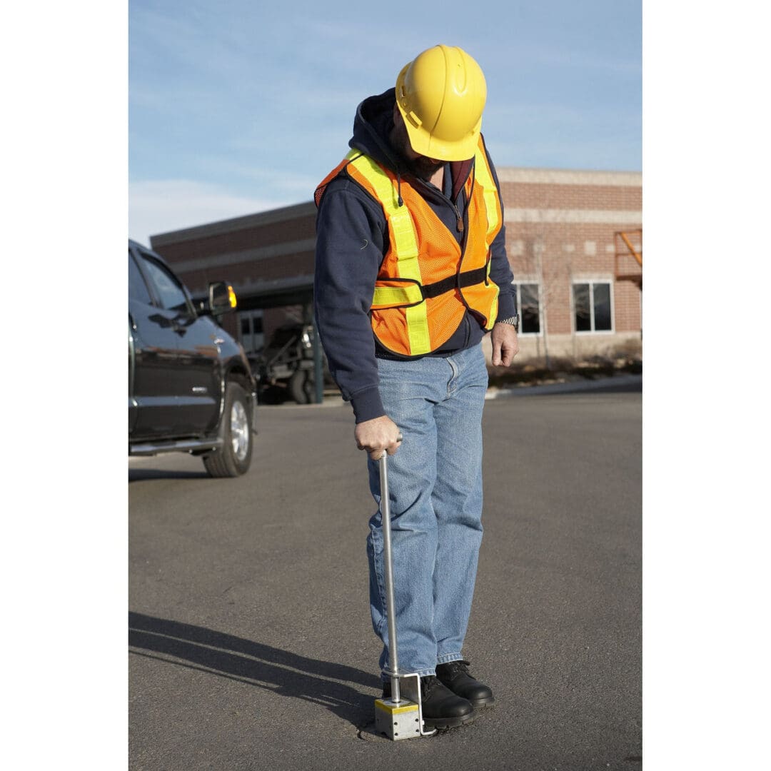 Worker using a magnetic sweeper on pavement.